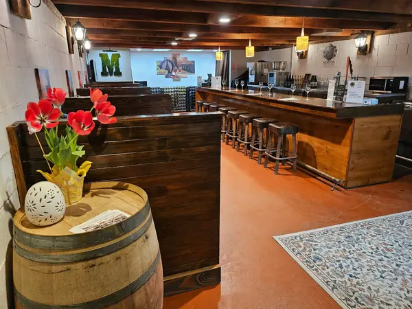 Interior view of the restored 1960s speakeasy tasting room at Morton Family Cellars — wooden booths, bar stools, and fresh tulips on a wine barrel in Apple Hill, Camino CA